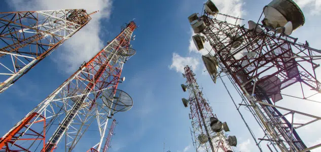 Several telecommunications towers with various antennas and satellite dishes stand tall against a blue sky with scattered clouds.